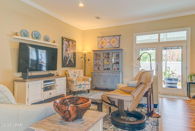 living area with ornamental molding, visible vents, and wood finished floors