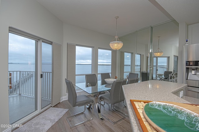 dining space with a water view, a towering ceiling, and light wood-style flooring