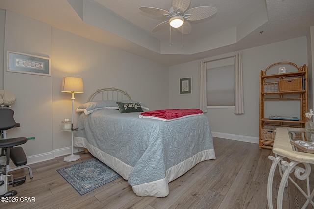 bedroom with light wood-style floors, ceiling fan, baseboards, and a raised ceiling