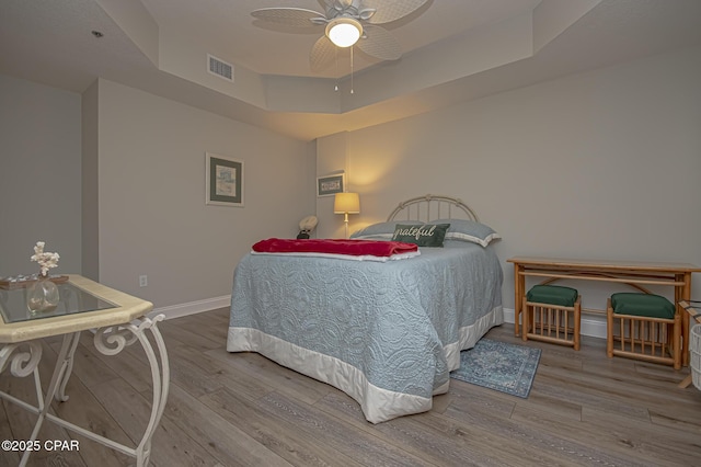 bedroom featuring wood finished floors, a raised ceiling, visible vents, and baseboards