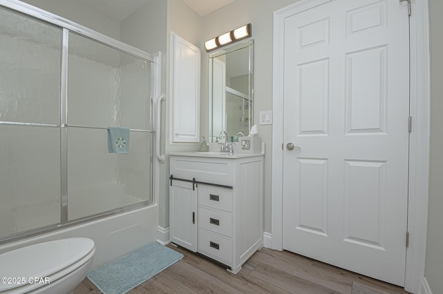 full bath with toilet, shower / bath combination with glass door, wood finished floors, and vanity