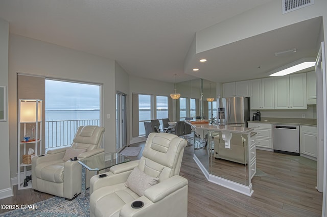 living area with light wood-style floors, recessed lighting, visible vents, and baseboards