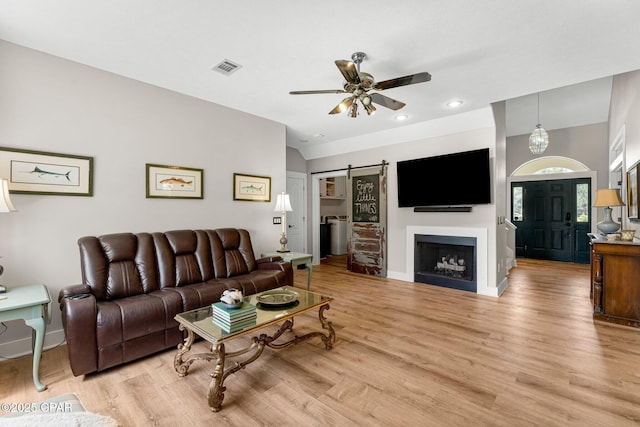 living room featuring light wood finished floors, ceiling fan, a barn door, and visible vents