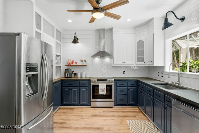 kitchen featuring tasteful backsplash, appliances with stainless steel finishes, wall chimney range hood, white cabinetry, and a sink