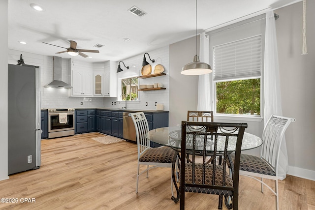 kitchen with light wood-style flooring, stainless steel appliances, visible vents, wall chimney exhaust hood, and tasteful backsplash