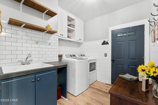 laundry area featuring washer and clothes dryer, cabinet space, light wood-style floors, a sink, and a textured ceiling