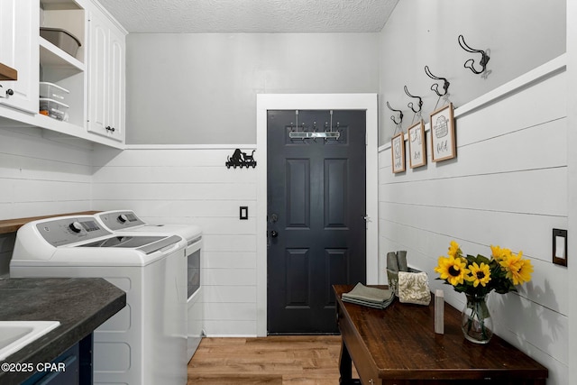 washroom with light wood-type flooring, washer and dryer, cabinet space, and a textured ceiling