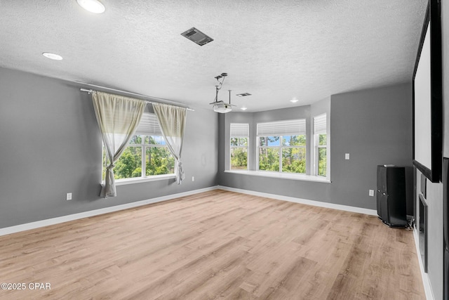 unfurnished living room featuring light wood-style floors, baseboards, visible vents, and a textured ceiling