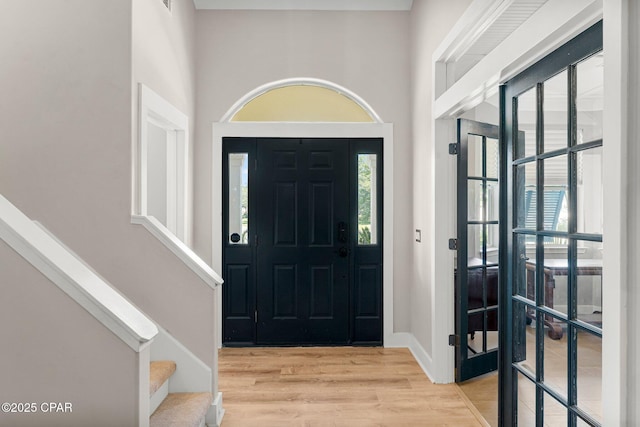 foyer featuring light wood-type flooring, plenty of natural light, stairway, and baseboards