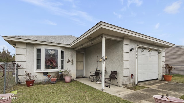 entrance to property with roof with shingles, an attached garage, fence, a yard, and stucco siding