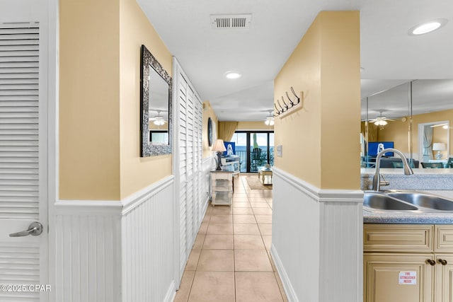 hall with a wainscoted wall, light tile patterned floors, a sink, and visible vents