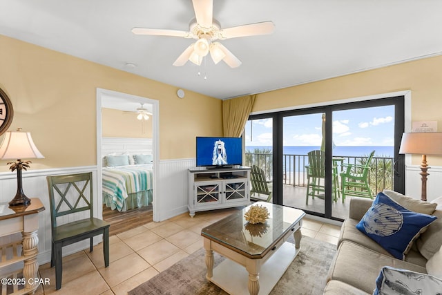 living area with light tile patterned floors, ceiling fan, and wainscoting