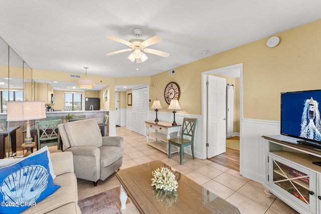 living room with a ceiling fan, wainscoting, visible vents, and light tile patterned floors