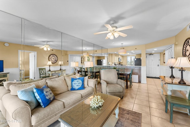 living area with ceiling fan, wainscoting, light tile patterned flooring, and visible vents