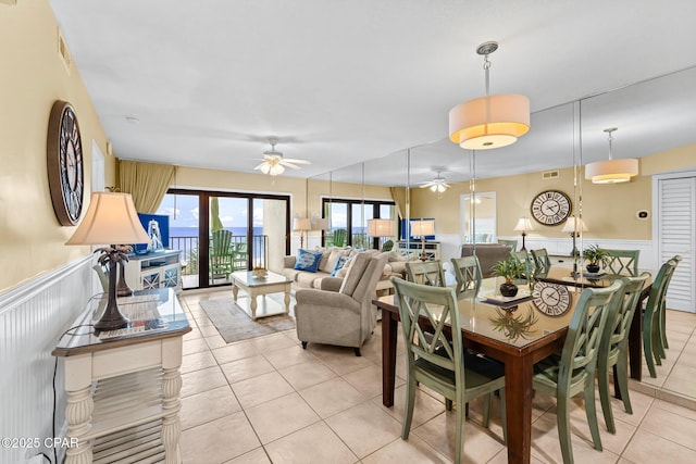 dining space with a wainscoted wall, ceiling fan, visible vents, and light tile patterned floors