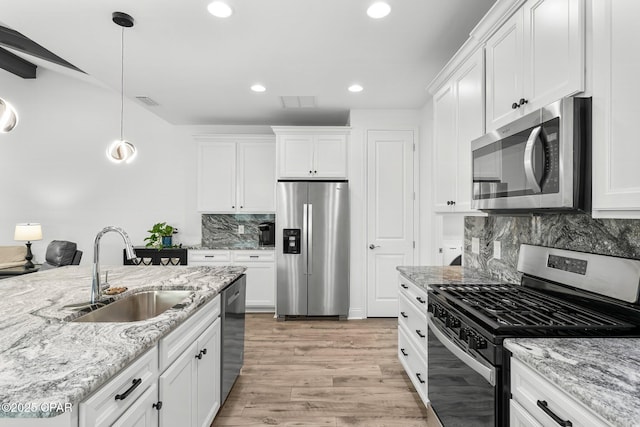 kitchen with white cabinets, appliances with stainless steel finishes, a sink, light wood-style flooring, and decorative light fixtures