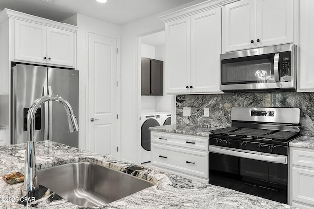 kitchen with washing machine and clothes dryer, appliances with stainless steel finishes, a sink, light stone counters, and white cabinetry