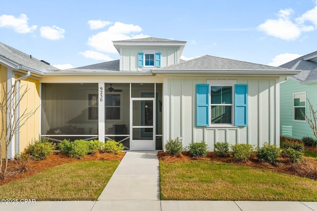 view of front of home with a sunroom, a shingled roof, a front lawn, and board and batten siding