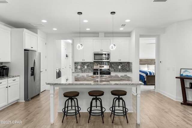 kitchen with visible vents, decorative backsplash, a kitchen breakfast bar, light wood-type flooring, and stainless steel appliances