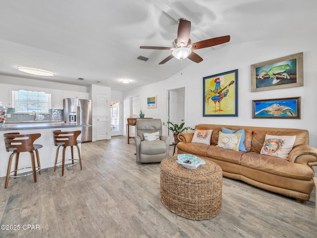 living area with a wealth of natural light, visible vents, lofted ceiling, and light wood finished floors