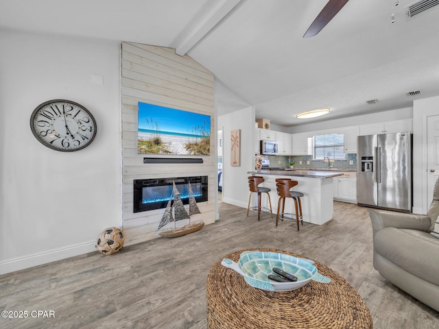 living area with visible vents, vaulted ceiling with beams, baseboards, light wood-type flooring, and a fireplace