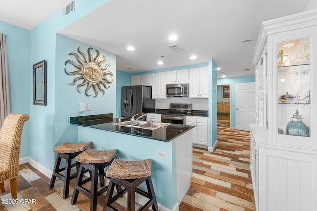 kitchen featuring visible vents, a peninsula, a sink, stainless steel appliances, and a kitchen breakfast bar