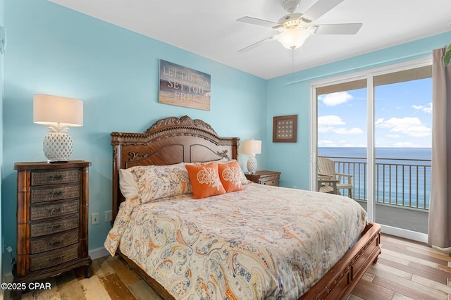 bedroom featuring a water view, a ceiling fan, wood finished floors, baseboards, and access to exterior