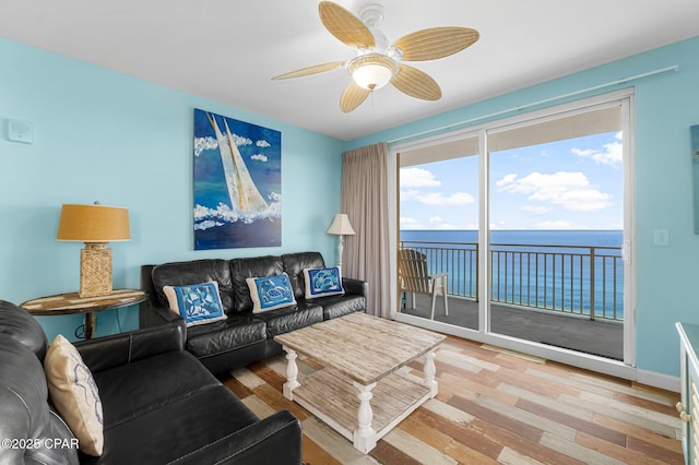 living room with baseboards, a water view, wood finished floors, and a ceiling fan