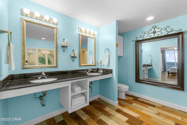 bathroom with toilet, wood finished floors, baseboards, and a sink