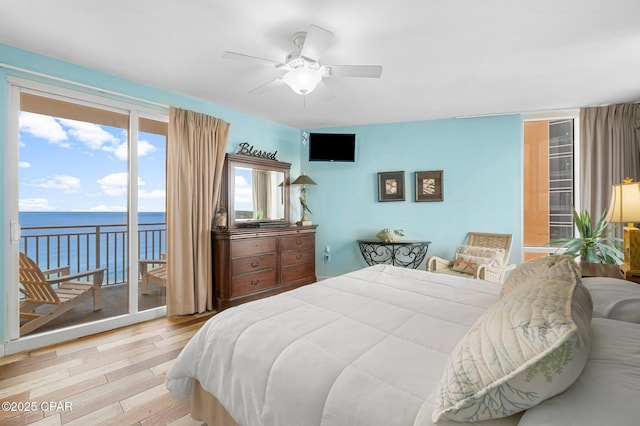 bedroom featuring a ceiling fan, access to exterior, wood finished floors, and a water view