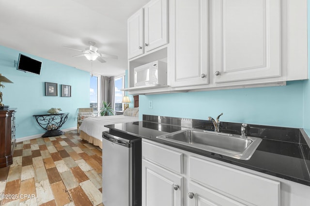 kitchen featuring dark countertops, dishwashing machine, white cabinets, a ceiling fan, and a sink