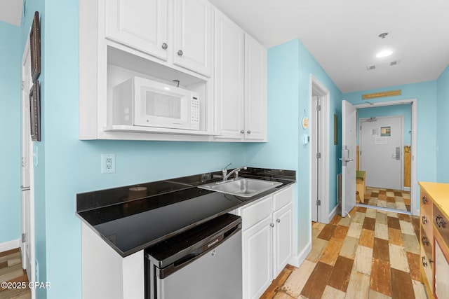 kitchen with white microwave, dark countertops, dishwasher, white cabinets, and a sink