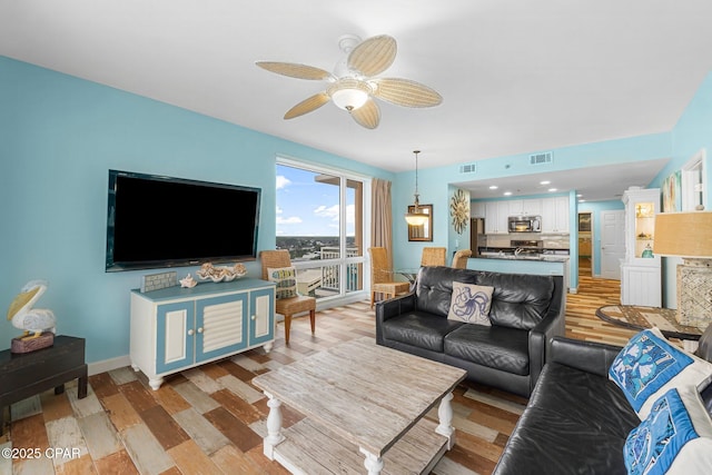 living area with light wood-type flooring, visible vents, baseboards, and a ceiling fan