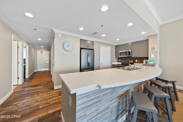 kitchen with gray cabinetry, stainless steel appliances, a peninsula, a kitchen breakfast bar, and light countertops