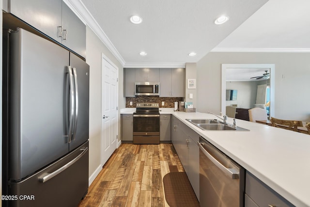 kitchen with gray cabinetry, stainless steel appliances, a sink, light countertops, and ornamental molding