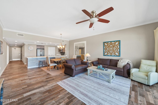 living room with baseboards, visible vents, ornamental molding, wood finished floors, and ceiling fan with notable chandelier