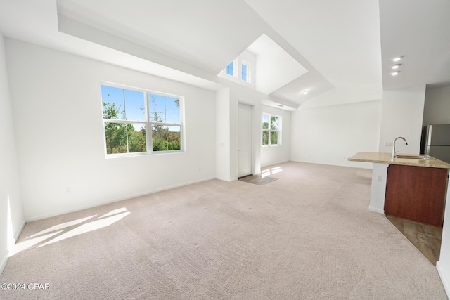 unfurnished living room with lofted ceiling, a sink, and light colored carpet