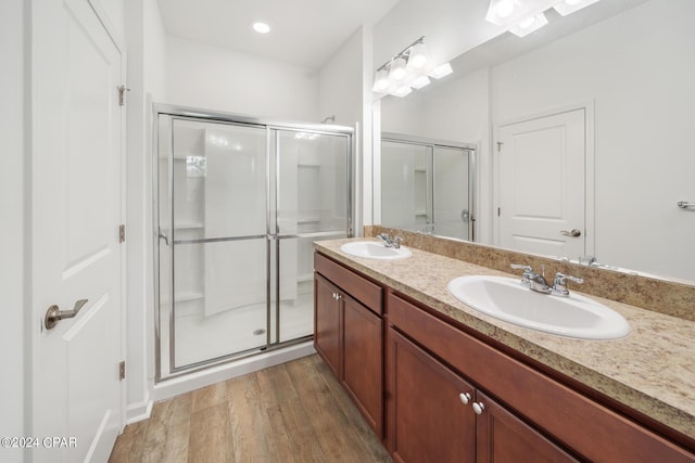 full bathroom featuring double vanity, a shower stall, a sink, and wood finished floors