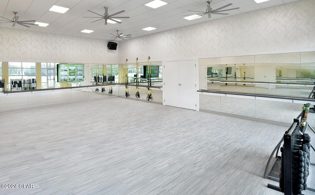 exercise room with a drop ceiling, ceiling fan, and a towering ceiling