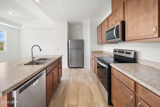 kitchen with stainless steel appliances, light countertops, light wood-style flooring, brown cabinetry, and a sink