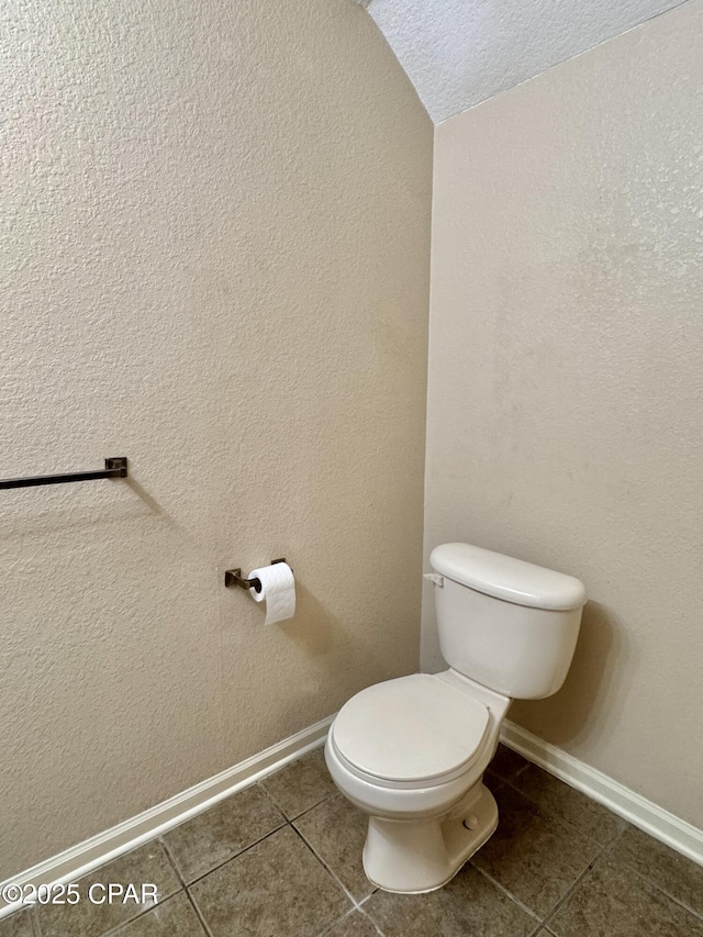 bathroom with a textured wall, tile patterned flooring, toilet, and baseboards