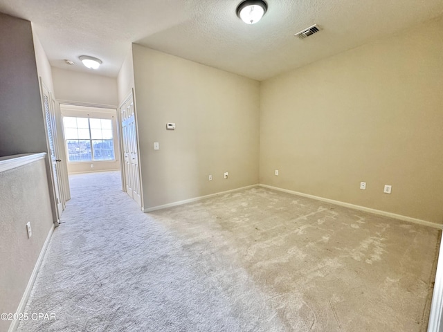 spare room with baseboards, visible vents, a textured ceiling, and light colored carpet