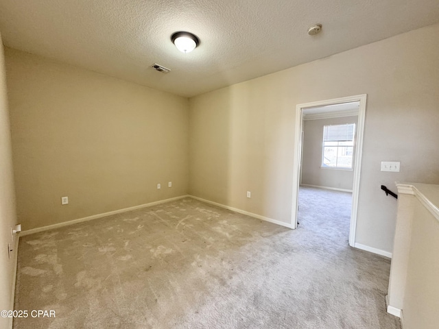 spare room with light colored carpet, visible vents, baseboards, and a textured ceiling