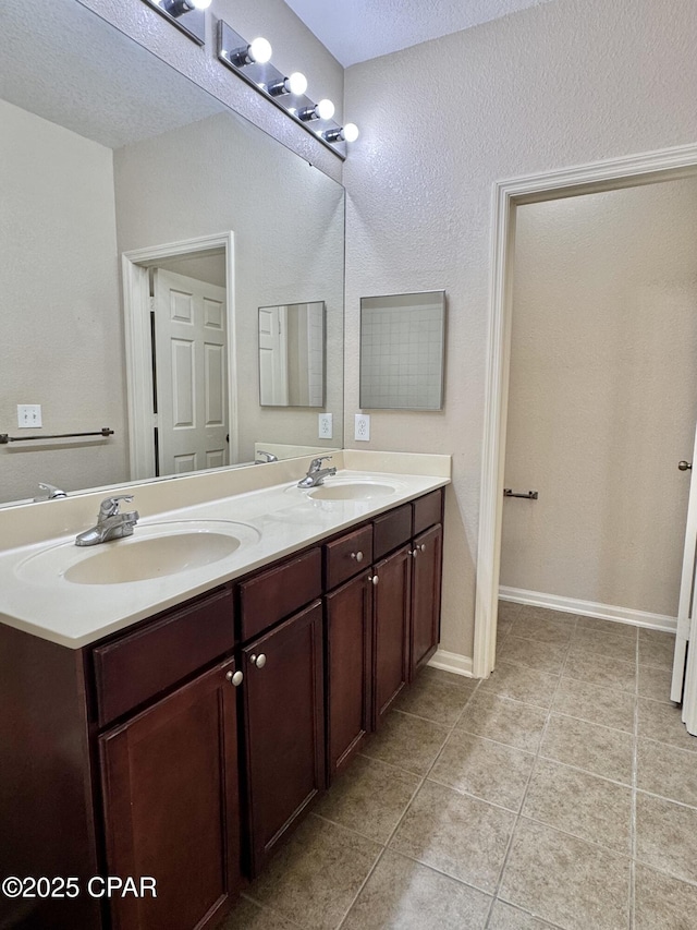 full bathroom with double vanity, tile patterned floors, a sink, and baseboards