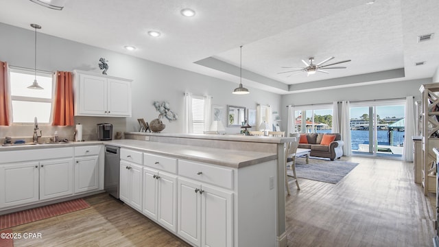 kitchen featuring a peninsula, a sink, white cabinets, open floor plan, and a raised ceiling