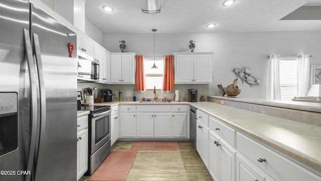 kitchen with stainless steel appliances, a sink, white cabinets, light countertops, and decorative light fixtures