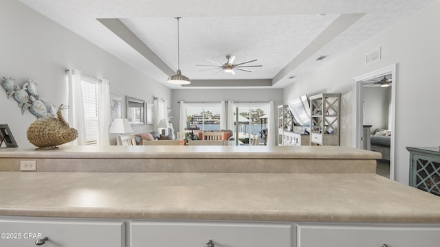 interior space featuring visible vents, a textured ceiling, a tray ceiling, and a ceiling fan