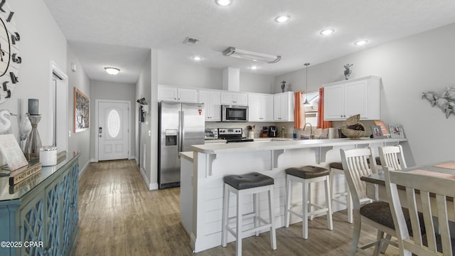 kitchen with a peninsula, a breakfast bar, white cabinetry, light countertops, and appliances with stainless steel finishes