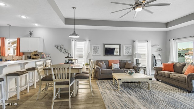 living room with ceiling fan, a tray ceiling, and dark wood-type flooring