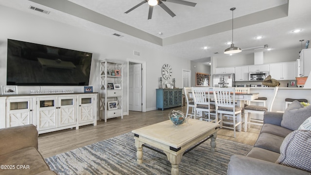 living area with light wood finished floors, visible vents, and a raised ceiling